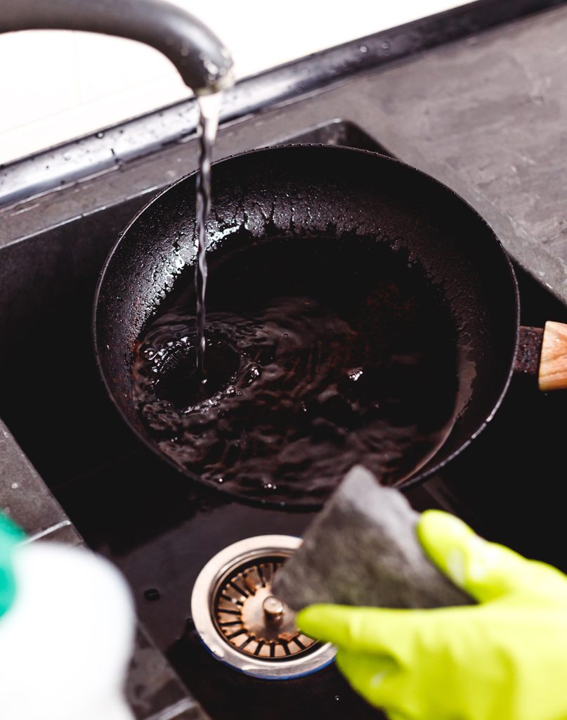 Person washing a dirty frying pan in the sink
